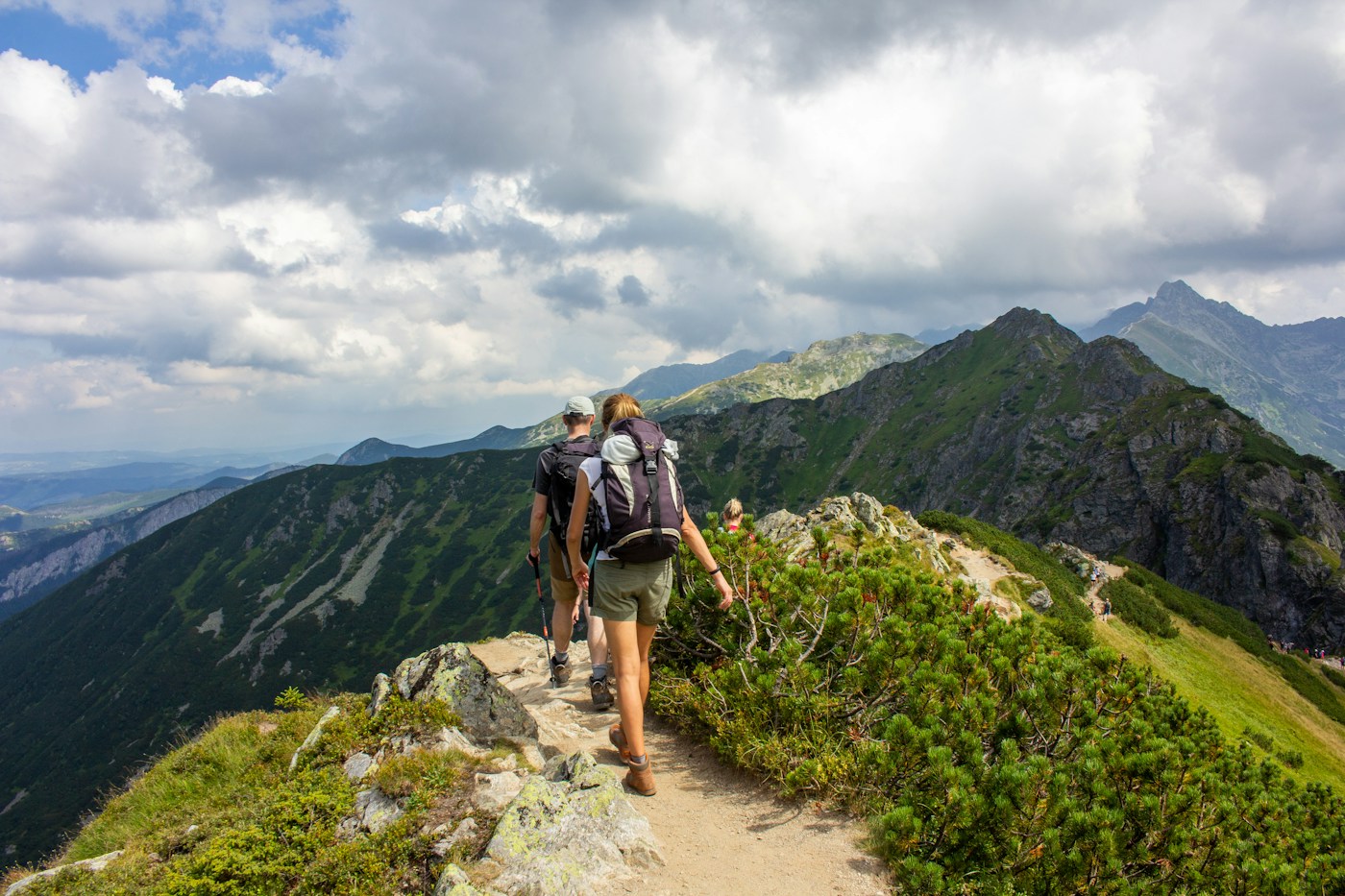 Two hikers following a mountain ridge trail toward a peak
