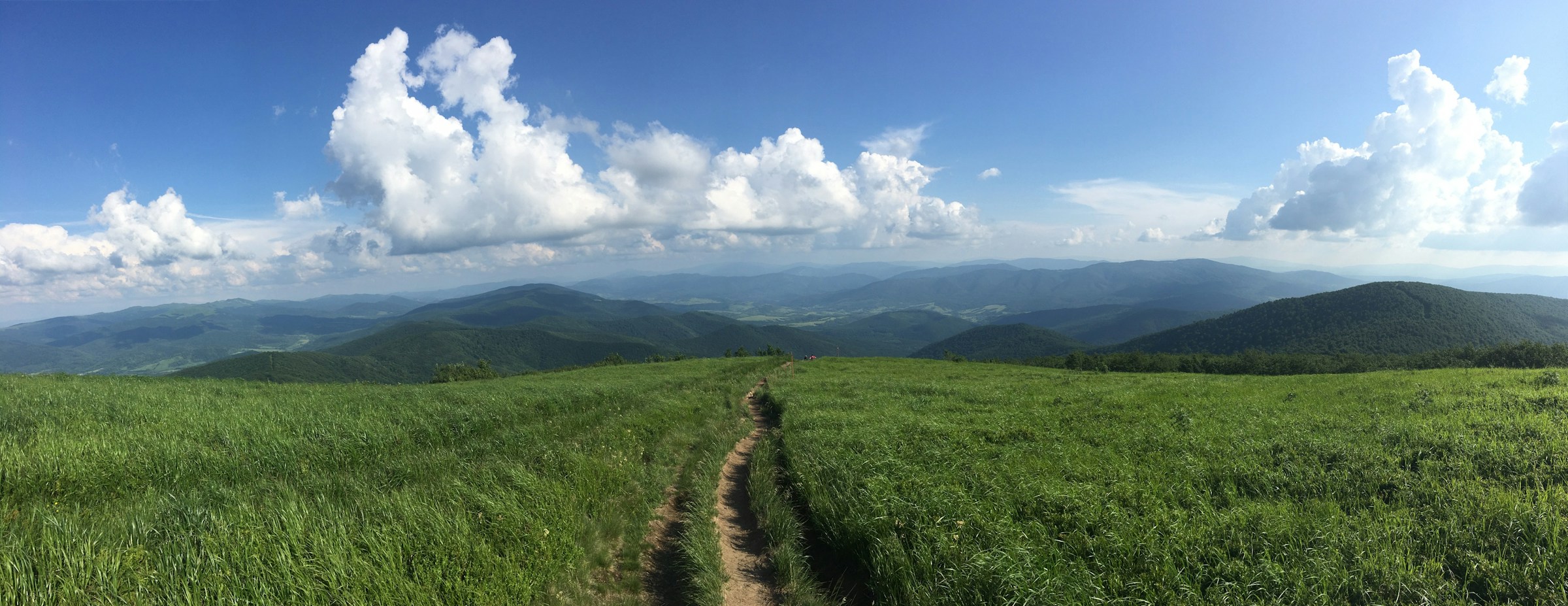 A winding path through green mountain meadows beneath an open sky